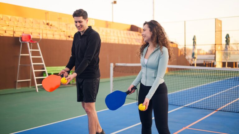 Two beginners smiling with pickleball paddles and balls on an outdoor court