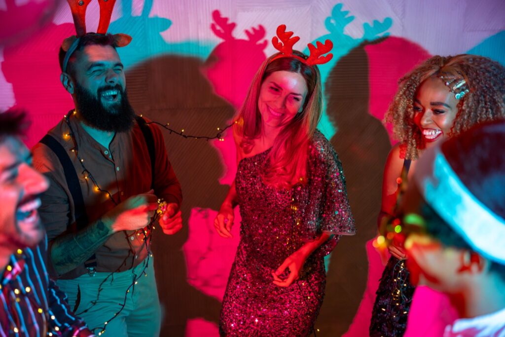Coworkers laughing together in reindeer antlers and string lights at a company holiday party