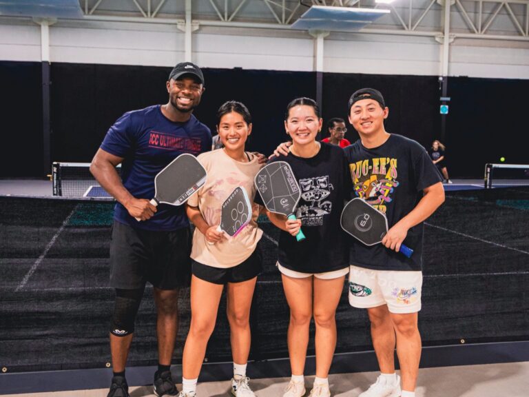 Four friends smiling with pickleball paddles at a group party at Texas Pickle Hall